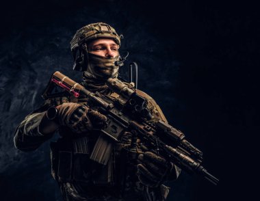Asker kamuflaj bir saldırı tüfeği tutan tek tip içinde tam donanımlı. Karanlık bir duvara Studio fotoğraf