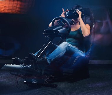 VR kulaklık takan bir kadın araba yarışı simülatörü kokpitinde koltuk ve tekerlekle araba sürüyor..