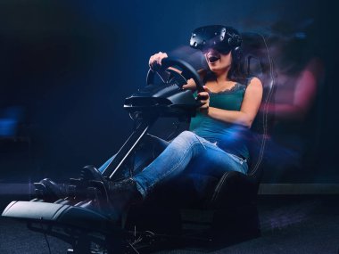 VR kulaklık takan genç bir kadın araba yarışları simülatörü kokpitinde otururken eğleniyor..