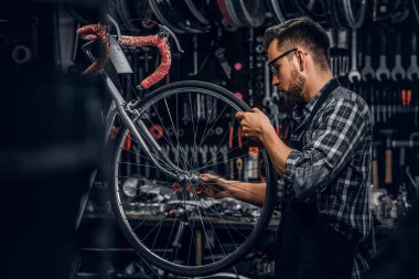 Koruyucu gözlüklü çekici dalgın adam kendi atölyesinde bisiklet tamir ediyor