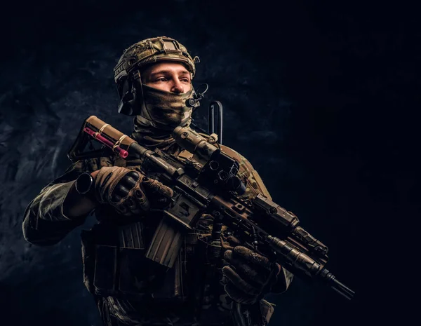 Soldado totalmente equipado con uniforme de camuflaje que sostiene un rifle de asalto. Foto del estudio contra una pared oscura —  Fotos de Stock