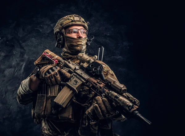 Soldado totalmente equipado con uniforme de camuflaje que sostiene un rifle de asalto. Foto del estudio contra una pared oscura —  Fotos de Stock