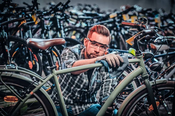 Привлекательный задумчивый мужчина в защитных очках чистит велосипед в собственном магазине . — стоковое фото