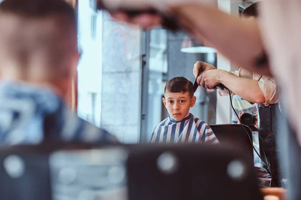 Pequeno menino da escola bonita teve seu primeiro corte de cabelo na moda na barbearia moderna — Fotografia de Stock