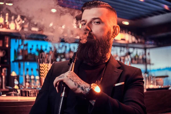 Retrato de homem tatuado barbudo que está fumando narguilé, fazendo bom vapor — Fotografia de Stock