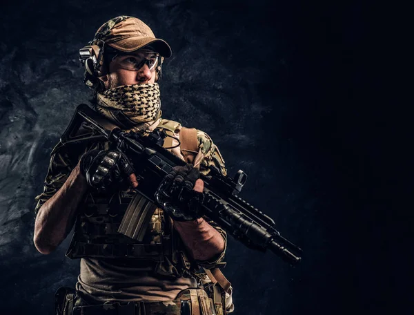 Soldado totalmente equipado con uniforme de camuflaje que sostiene un rifle de asalto. Foto del estudio contra una pared oscura —  Fotos de Stock