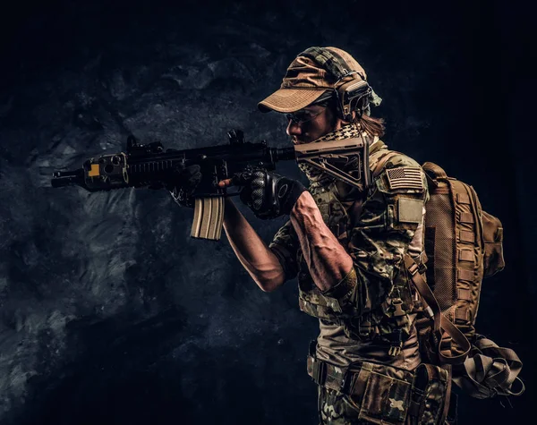 Elitní jednotka speciálních sil voják v uniformě kamufláž držení útočná puška s laserovým zaměřovačem a cíle na cíl. Studiové fotografie tmavé stěny — Stock fotografie