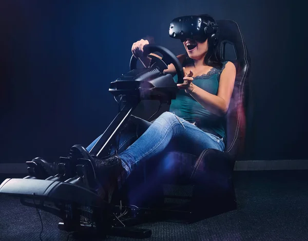 Jonge vrouw draagt Vr headset veel plezier tijdens het rijden op autoracesimulator cockpit met stoel en wiel. — Stockfoto