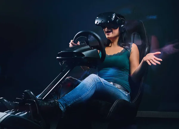 Jonge vrouw draagt Vr headset veel plezier tijdens het rijden op autoracesimulator cockpit met stoel en wiel. — Stockfoto