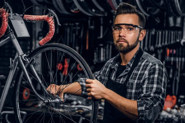 Atractivo hombre pensativo en gafas protectoras está reparando la bicicleta en su propio taller — Foto de Stock