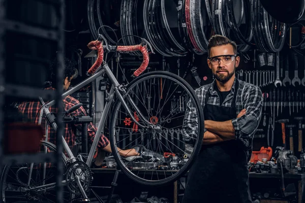 Handsome bearded man in glasses is standing near fixed bicycle at his own workshop