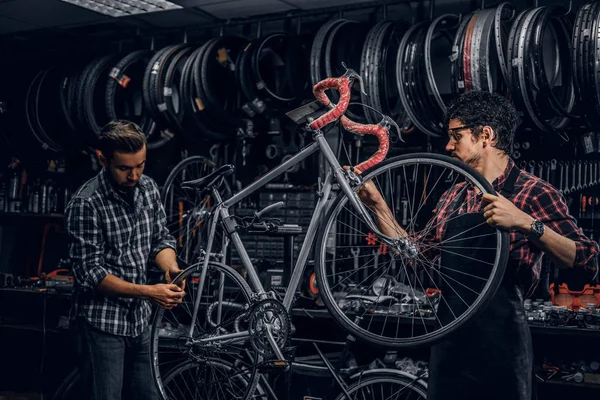 Dos hombres atractivos están trabajando en la fijación de bicicletas en el taller ocupado — Foto de Stock