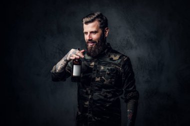 Askeri gömlek şık sakallı hipster adam zanaat bira tadı sahiptir. Koyu duvara karşı stüdyo fotoğrafı