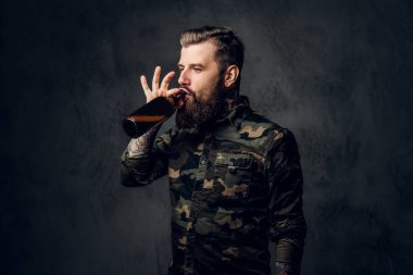 Askeri gömlek şık sakallı hipster adam zanaat bira tadı sahiptir. Koyu duvara karşı stüdyo fotoğrafı