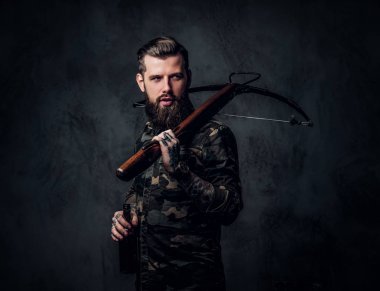 Askeri gömlek bir zanaat bira ve bir ortaçağ yay tutan şık sakallı hipster adam. Koyu duvara karşı stüdyo fotoğrafı