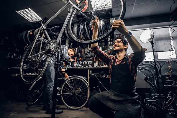 Dos reparadores atractivos están arreglando la bicicleta rota en su taller oscuro — Foto de Stock