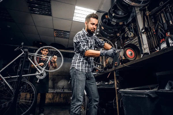 O homem atraente está trabalhando com a máquina na oficina ocupada da bicicleta . — Fotografia de Stock