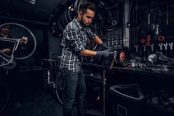 Hombre atractivo está trabajando con la máquina en el taller de bicicletas ocupado . —  Fotos de Stock