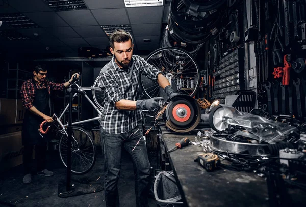 O homem atraente está trabalhando com a máquina na oficina ocupada da bicicleta . — Fotografia de Stock