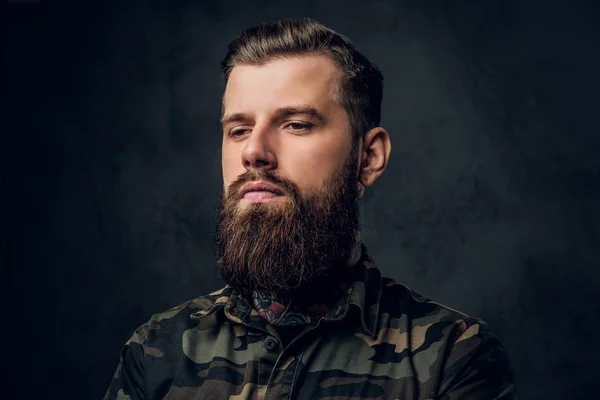 Ritratto ravvicinato di un giovane tatuato con barba e acconciatura. Studio foto contro muro scuro — Foto Stock