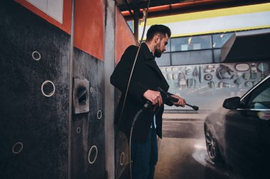 Kot pantolon ve blaser Akıllı trendy adam araba yıkama istasyonunda kendi araba yıkıyor