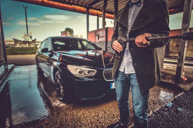 Bakımlı adam arabasının yanındaki araba yıkama istasyonunda hortumla poz verdi..