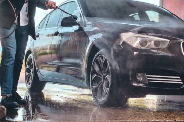 Meşgul adam araba yıkama istasyonunda kendi arabasını yıkıyor.