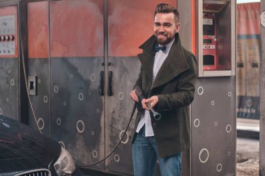 Çekici adam arabasının yakınındaki araba yıkama istasyonunda hortumla poz.