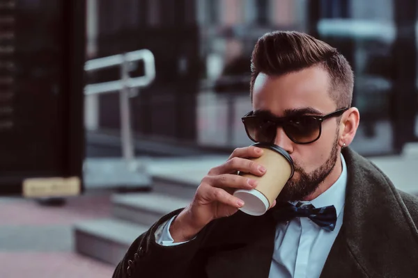 Atractivo hombre elegante en gafas de sol está bebiendo su café mientras está sentado fuera en coffeeshop — Foto de Stock