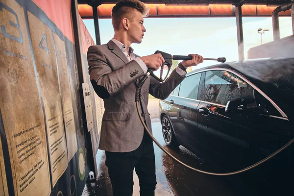Młody mężczyzna myje własny samochód w myjni samochodowej. — Zdjęcie stockowe