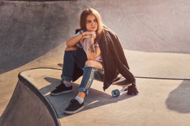 Uzun saçlı trendy kadın onu longboard üzerinde skatepark oturuyor.