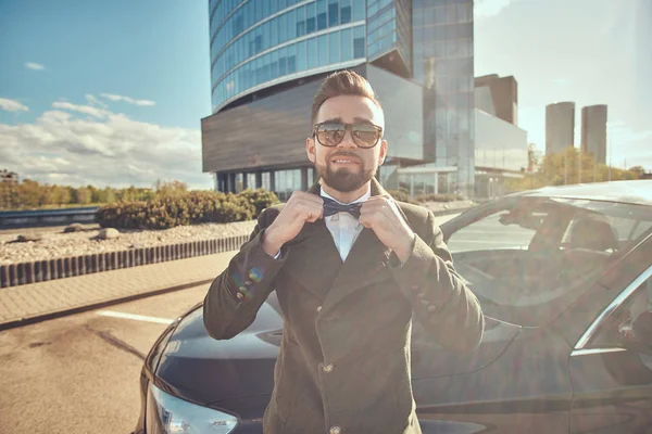 Hombre feliz en abrigo está de pie cerca de su nuevo coche en el aparcamiento . — Foto de Stock