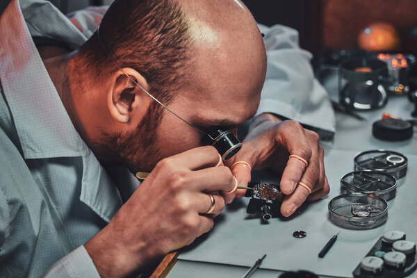 Expirienced clockmaster is fixing old watch for a customer at his repairing workshop