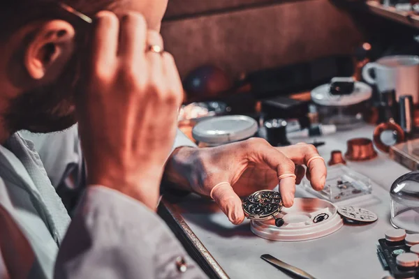 Reloj maduro está fijando viejo reloj para un cliente en su taller de reparación ocupado — Foto de Stock