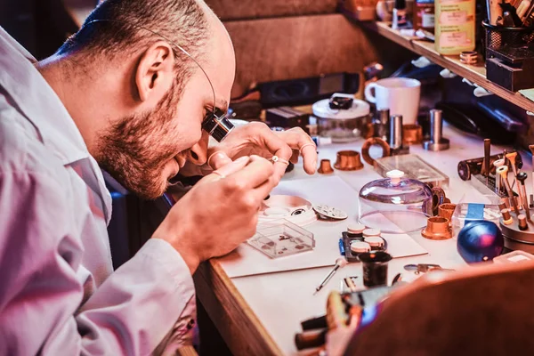 Clockmaster maturo sta fissando vecchio orologio per un cliente presso la sua officina di riparazione occupato — Foto Stock