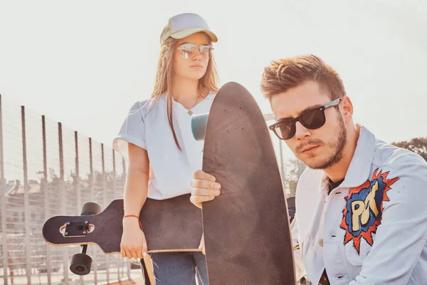 Mladý trendy pár je chilling na slunné ulici s jejich longboardy — Stock fotografie