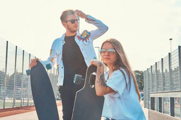 Vonzó fiatal pár pihentető a napsütötte utcán a longboards — Stock Fotó