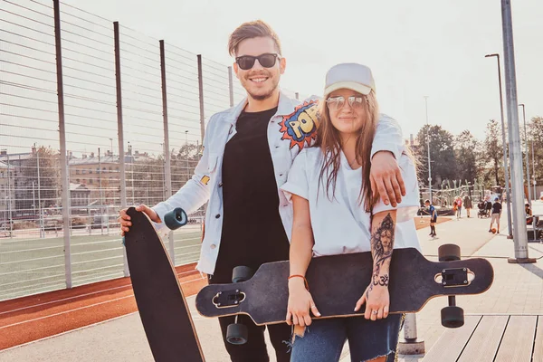 Feliz casal sorrindo está de pé na rua de verão com seus longboards — Fotografia de Stock