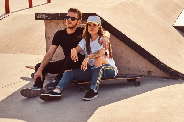 Mladí trendy pár sedí na slunné skatepark se svými longboardy — Stock fotografie