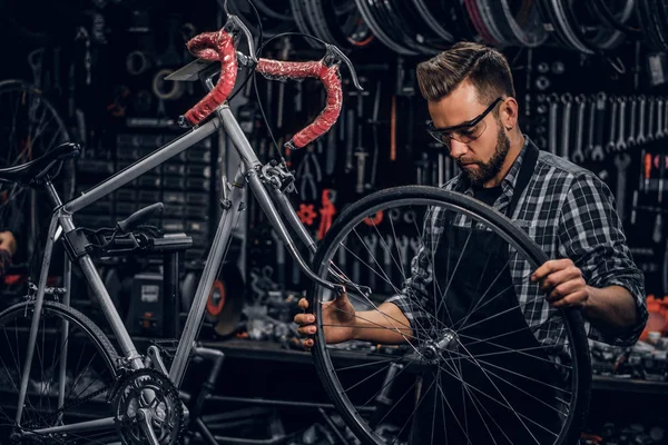 Guapo hombre serio en gafas protectoras es la fijación de la bicicleta en su propia tienda — Foto de Stock