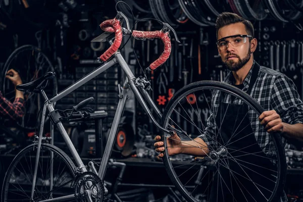 Handsome serious man in protective glasses is fixing bicycle at his own shop
