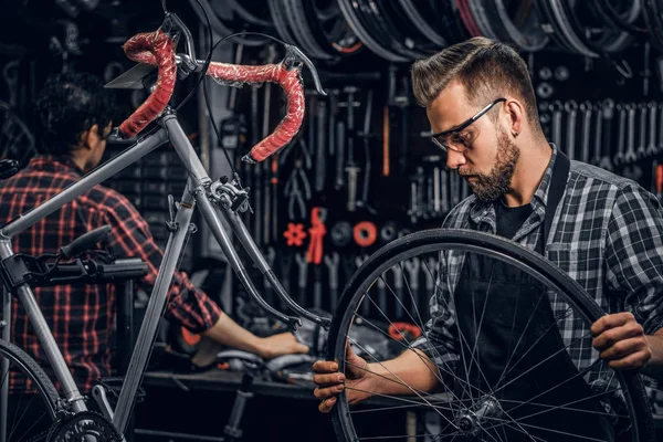 Enfocado hombre atractivo en gafas es chainging rueda para bicicleta en taller ocupado — Foto de Stock
