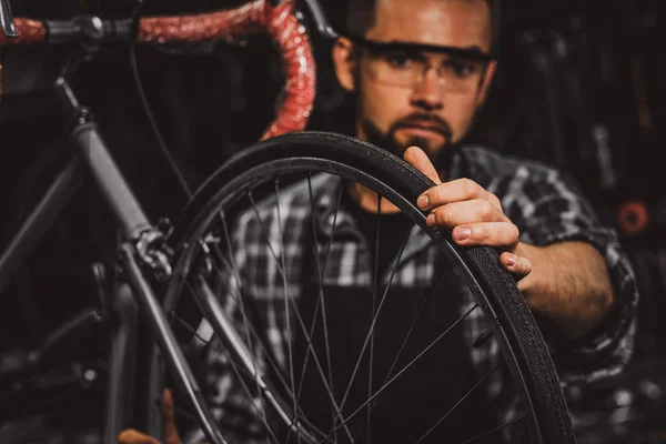 Guapo hombre serio en gafas protectoras es la fijación de la bicicleta en su propia tienda — Foto de Stock