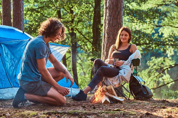 Couple of young students are chilling near bonfire in the green forest