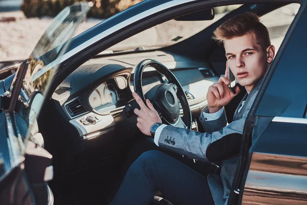 Mladý podnikatel sedí ve svém autě na parkovišti a mluví přes mobilní telefon. — Stock fotografie