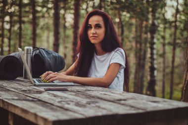 Neşeli öğrenci ormanın ortasında dizüstü bilgisayar üzerinde çalışıyor.