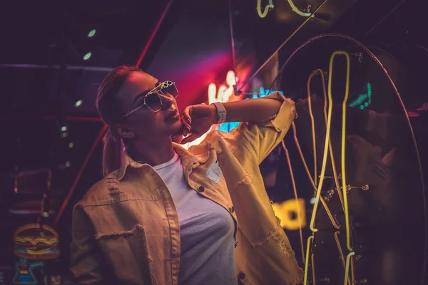 Atraktivní styltivá žena se pózuje pro fotografa v neonové světelné světlici. Na pozadí je tma. — Stock fotografie