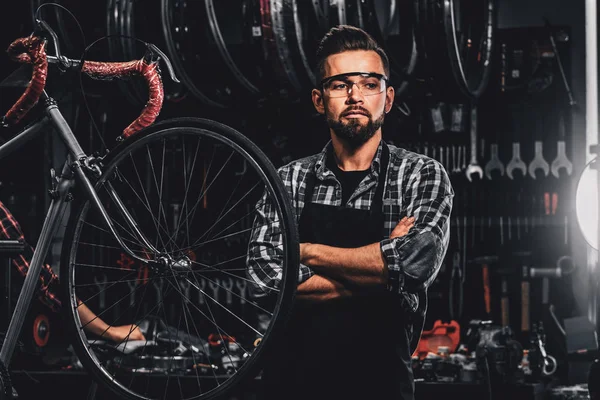 Handsome bearded man in glasses is standing near fixed bicycle at his own workshop