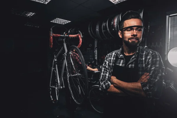 Handsome bearded man in glasses is standing near fixed bicycle at his own workshop