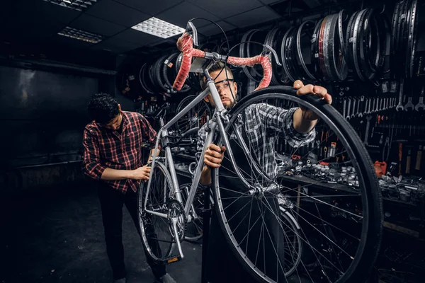 Two attractive mans are working on bicycle fixing at busy workshop